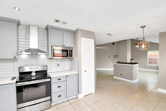 kitchen featuring pendant lighting, a textured ceiling, stainless steel appliances, decorative backsplash, and wall chimney exhaust hood