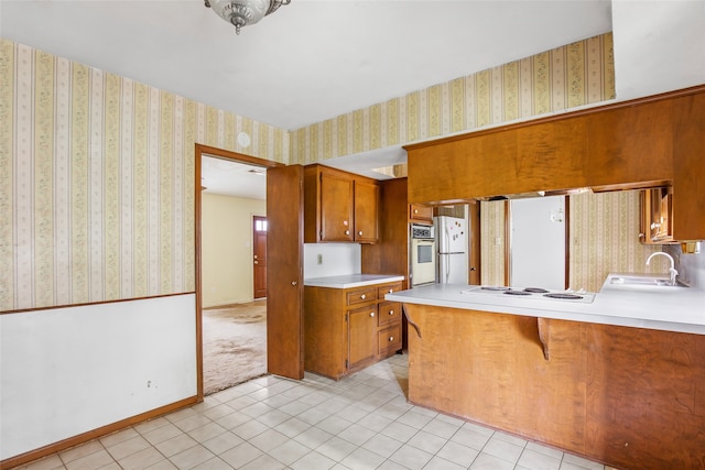 kitchen with white appliances, sink, kitchen peninsula, light tile patterned flooring, and a kitchen breakfast bar