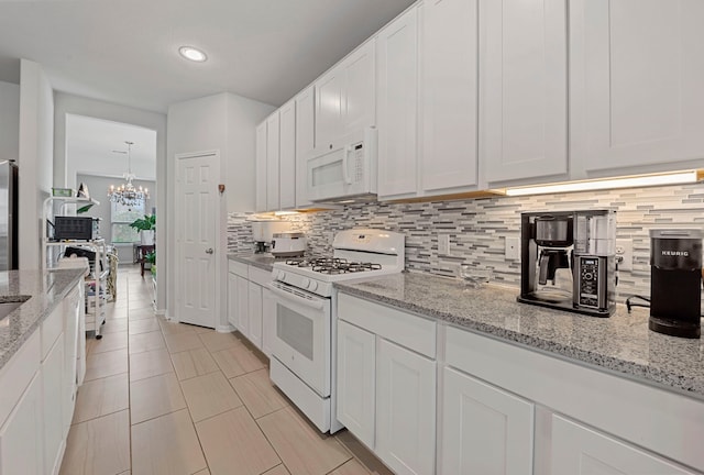 kitchen with backsplash, a notable chandelier, white appliances, and white cabinetry