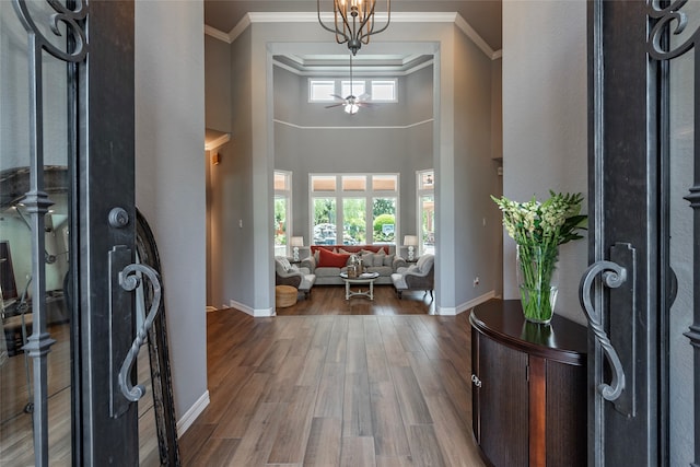 entryway with a high ceiling, hardwood / wood-style floors, ceiling fan with notable chandelier, and crown molding