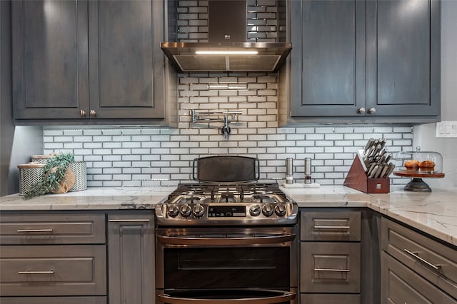 kitchen with light stone countertops, wall chimney exhaust hood, stainless steel gas range oven, and tasteful backsplash