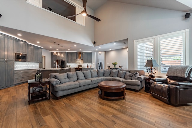 living room featuring high vaulted ceiling, ceiling fan, sink, and light hardwood / wood-style flooring