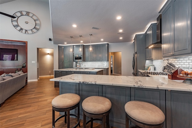 kitchen featuring wall chimney exhaust hood, pendant lighting, light hardwood / wood-style flooring, tasteful backsplash, and kitchen peninsula