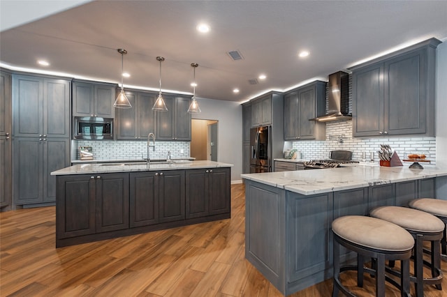 kitchen featuring light wood-type flooring, appliances with stainless steel finishes, light stone counters, and wall chimney range hood