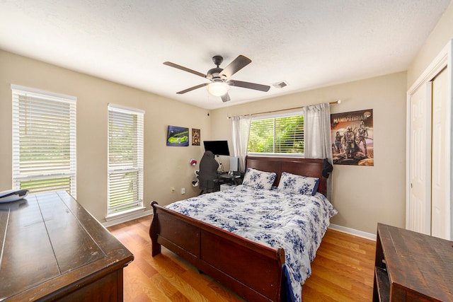 bedroom featuring baseboards, visible vents, ceiling fan, a textured ceiling, and light wood-style floors