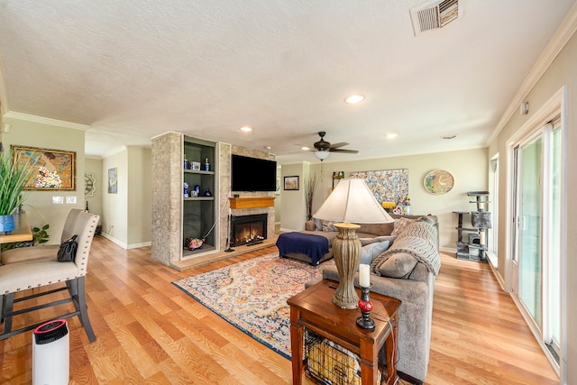 living area with crown molding, light wood-type flooring, visible vents, and a fireplace