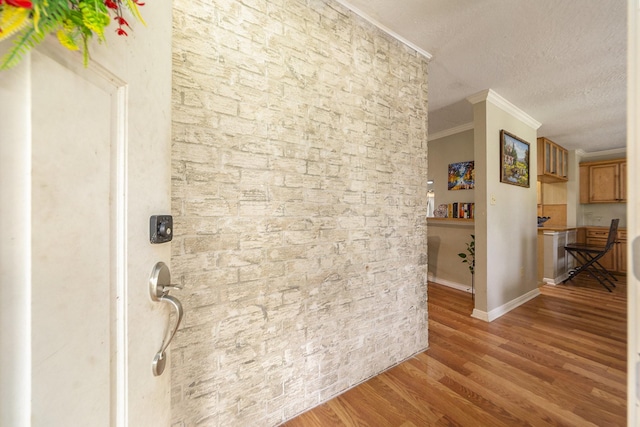 hall featuring crown molding, a textured ceiling, baseboards, and wood finished floors