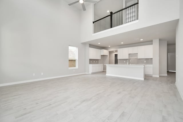 unfurnished living room featuring a towering ceiling, ceiling fan, and light hardwood / wood-style flooring