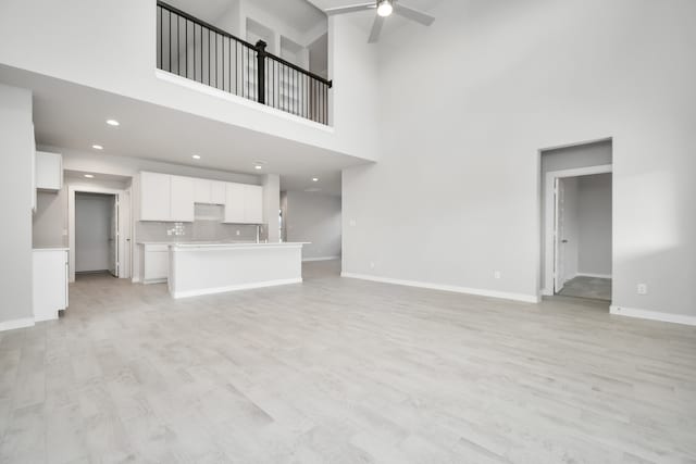 unfurnished living room with a high ceiling, ceiling fan, and light hardwood / wood-style flooring