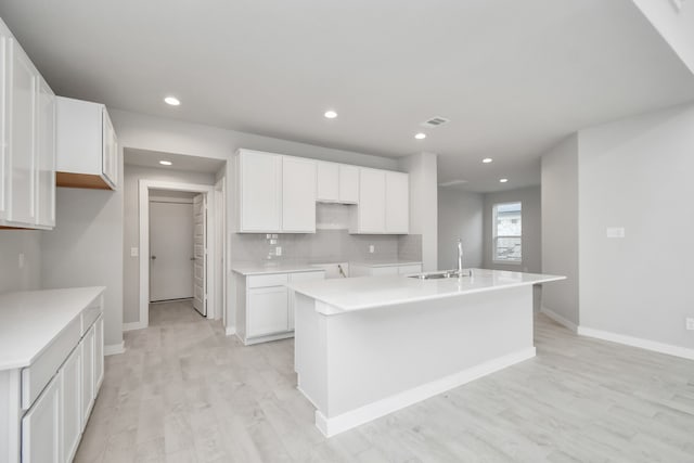 kitchen featuring an island with sink, light wood-type flooring, white cabinets, backsplash, and sink