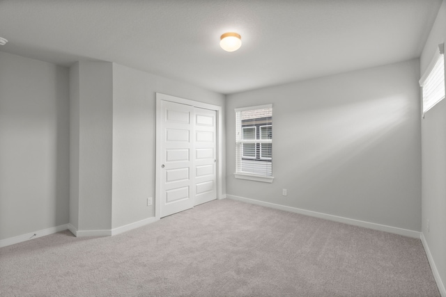 unfurnished bedroom with light colored carpet, a closet, and multiple windows