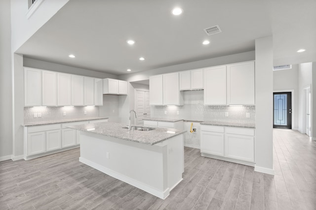 kitchen featuring sink, white cabinetry, light wood-type flooring, light stone countertops, and a center island with sink