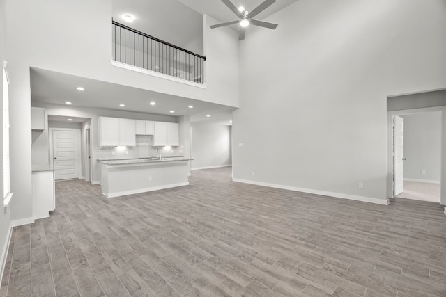 unfurnished living room featuring a towering ceiling, ceiling fan, and light hardwood / wood-style flooring