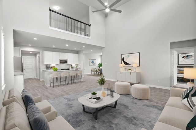 living room featuring a towering ceiling, ceiling fan, and light hardwood / wood-style floors