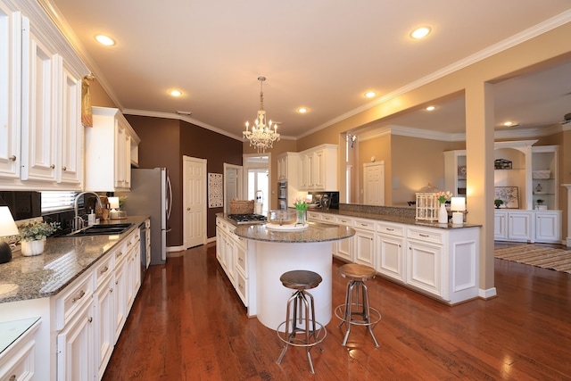 kitchen featuring a kitchen island, a sink, stainless steel appliances, white cabinetry, and dark wood-type flooring