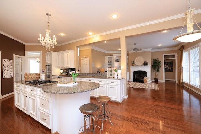 kitchen featuring appliances with stainless steel finishes, a fireplace, white cabinetry, dark wood-type flooring, and a kitchen island