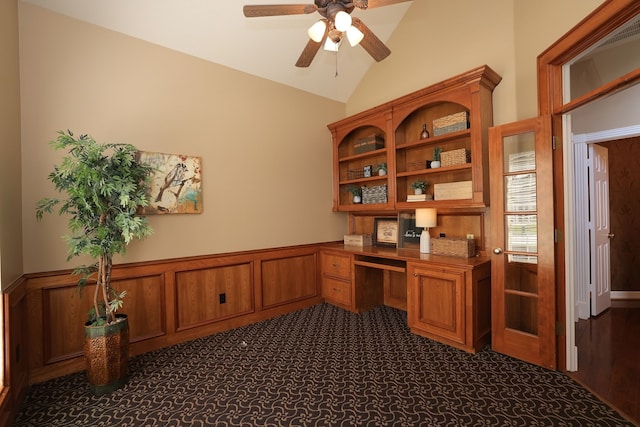 home office with a ceiling fan, built in desk, lofted ceiling, and a wainscoted wall
