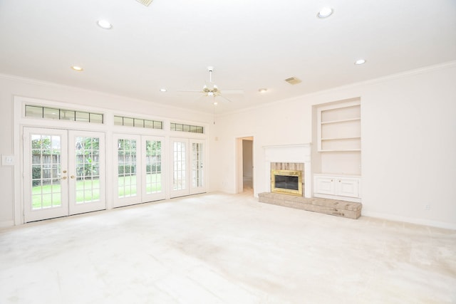 unfurnished living room with built in shelves, ceiling fan, a tile fireplace, and crown molding