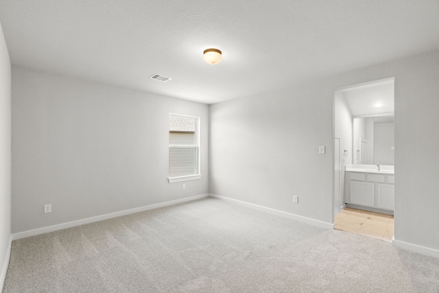 unfurnished bedroom with a textured ceiling, sink, light carpet, and ensuite bathroom