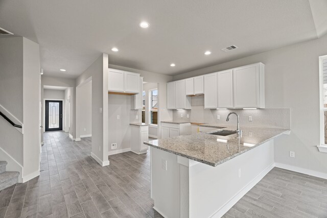 8427 Northern Pintail Dr, Houston, TX 77049 - kitchen featuring a sink, a peninsula, visible vents, light wood-style flooring, and light stone countertops