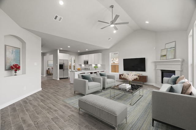 living room with light wood-type flooring, ceiling fan, high vaulted ceiling, and sink