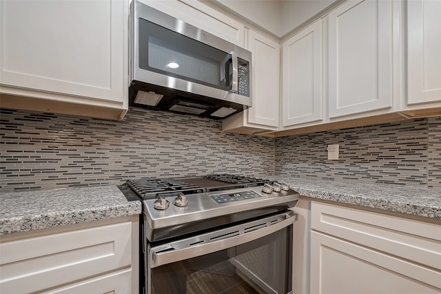 kitchen with appliances with stainless steel finishes, white cabinetry, light stone counters, and decorative backsplash