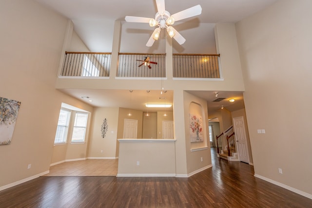 unfurnished living room featuring ceiling fan, dark hardwood / wood-style floors, and a towering ceiling