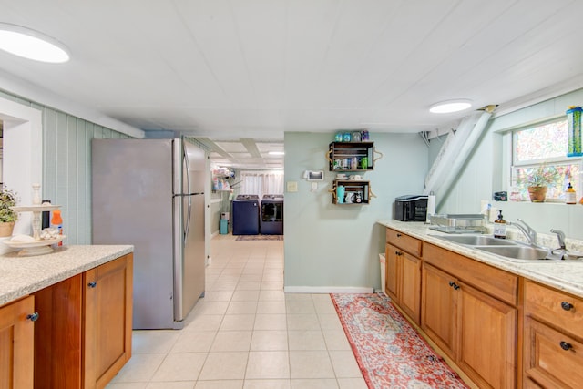 kitchen with washer and clothes dryer, stainless steel fridge, light tile patterned floors, light stone counters, and sink