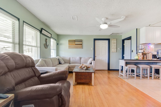 living room with a textured ceiling, ceiling fan, and light hardwood / wood-style floors