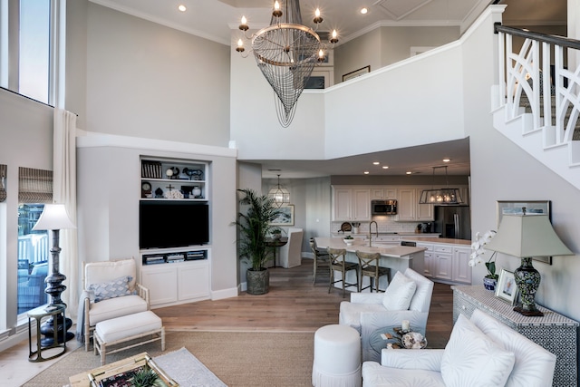 living room with hardwood / wood-style floors, a towering ceiling, ornamental molding, and an inviting chandelier