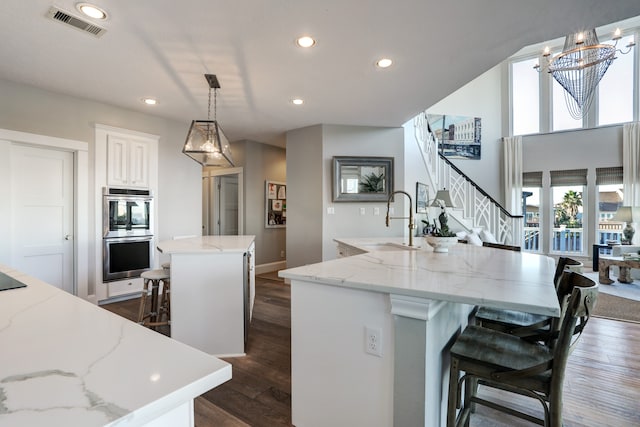 kitchen with a kitchen island with sink, sink, hanging light fixtures, stainless steel double oven, and a breakfast bar area