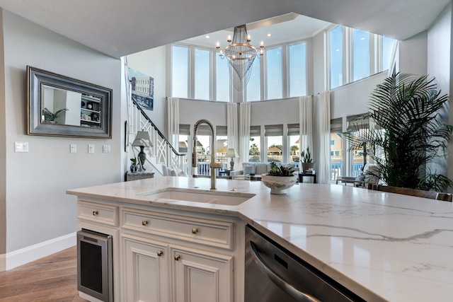 kitchen with light stone countertops, white cabinetry, sink, hanging light fixtures, and light wood-type flooring