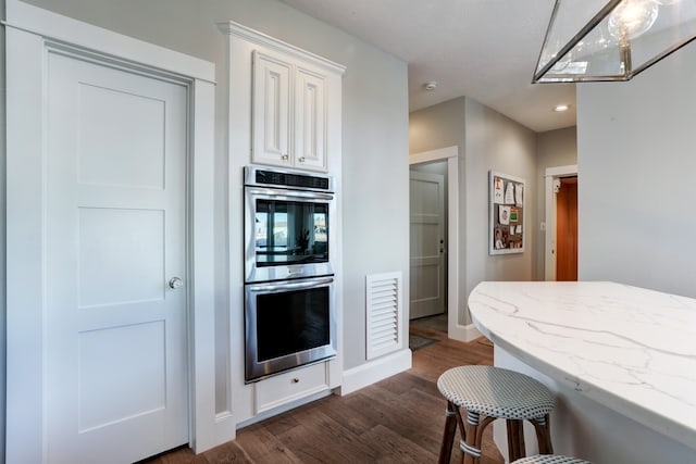 kitchen featuring light stone countertops, a kitchen breakfast bar, double oven, white cabinets, and dark hardwood / wood-style floors