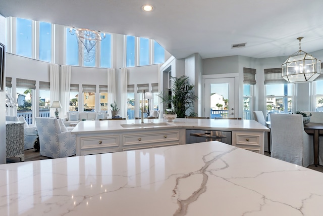 kitchen featuring decorative light fixtures, light stone counters, sink, and a wealth of natural light