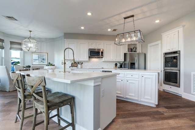 kitchen featuring dark wood-type flooring, stainless steel appliances, an island with sink, decorative light fixtures, and white cabinets