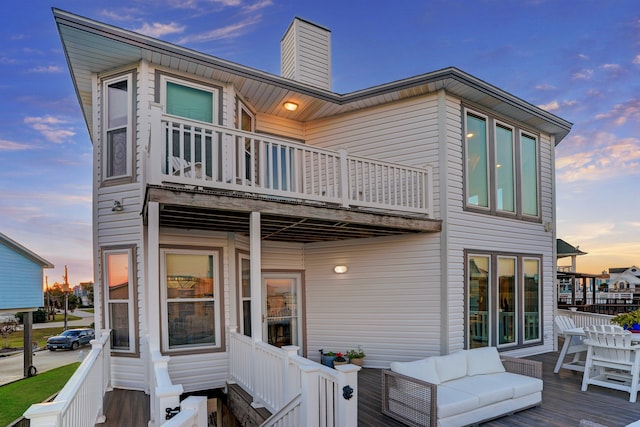 back house at dusk with a balcony and a wooden deck