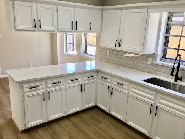 kitchen featuring light stone countertops, decorative backsplash, kitchen peninsula, and sink