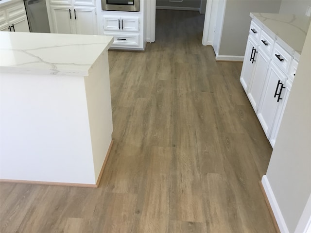 kitchen featuring wood-type flooring, light stone countertops, and white cabinetry