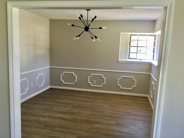 empty room featuring hardwood / wood-style flooring, a chandelier, and a textured ceiling