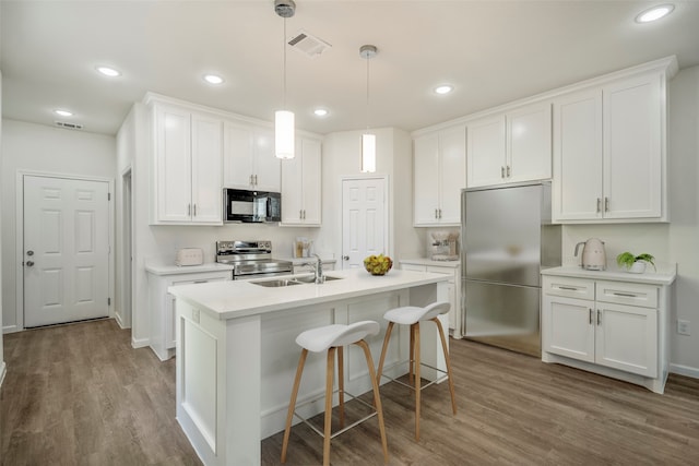 kitchen featuring light hardwood / wood-style flooring, decorative light fixtures, stainless steel appliances, white cabinetry, and a center island with sink