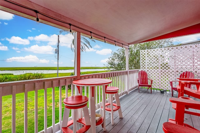 wooden terrace featuring a water view and a lawn