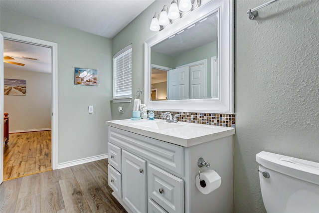 bathroom featuring toilet, wood-type flooring, ceiling fan, decorative backsplash, and vanity