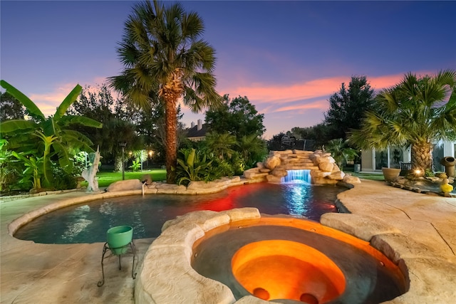 pool at dusk featuring an in ground hot tub, a patio, and pool water feature