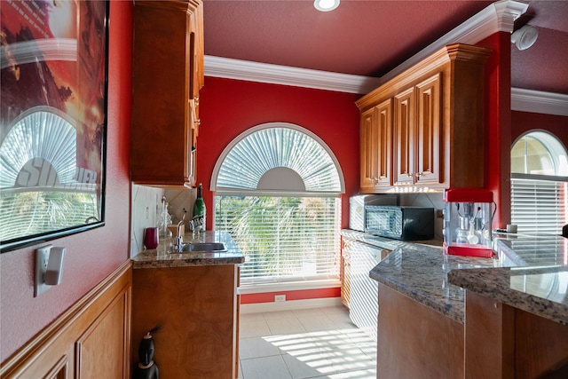 kitchen with backsplash, dark stone counters, ornamental molding, sink, and light tile patterned floors