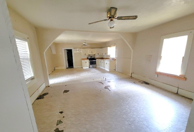 unfurnished living room featuring ceiling fan, light floors, arched walkways, and a sink