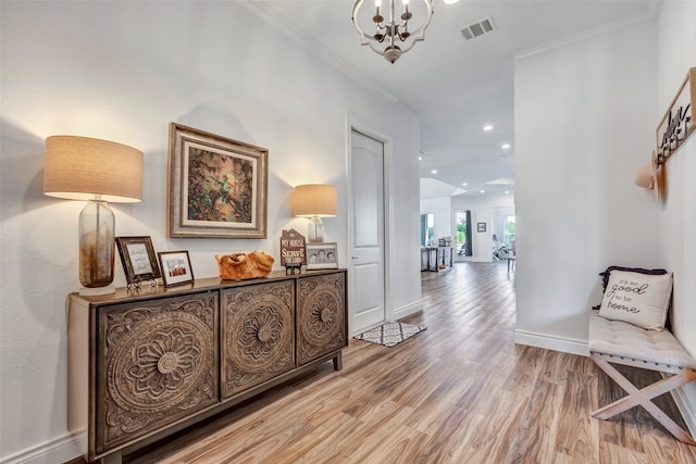 hallway with light wood-type flooring, crown molding, and an inviting chandelier