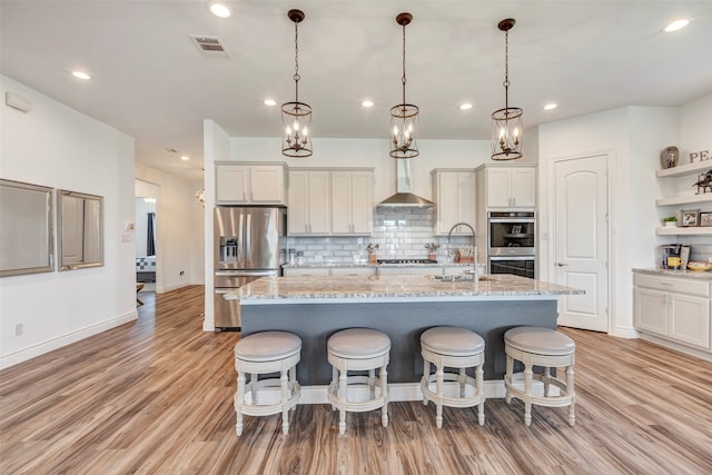 kitchen with appliances with stainless steel finishes, a center island with sink, decorative backsplash, and light hardwood / wood-style flooring