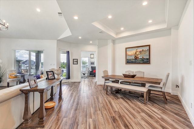 dining space with wood-type flooring, a tray ceiling, and a wealth of natural light