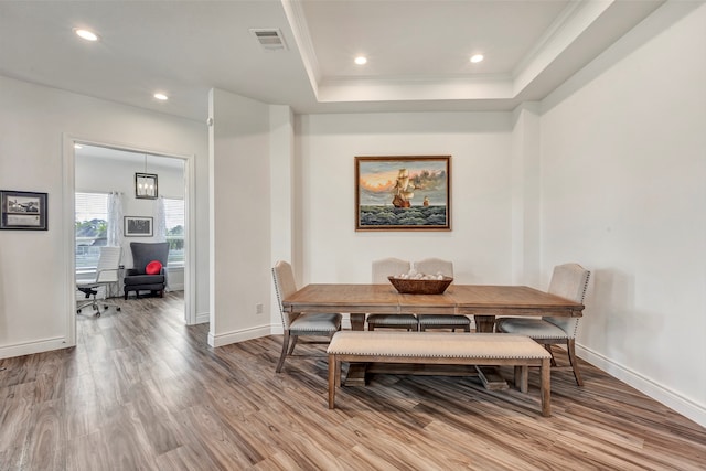 dining room featuring wood-type flooring, a raised ceiling, and crown molding