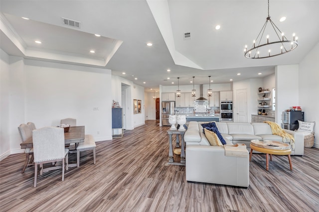 living room with an inviting chandelier, a tray ceiling, light hardwood / wood-style floors, and ornamental molding